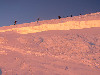 The crowded line of climbers moving further, with a crevasse in the foreground.
