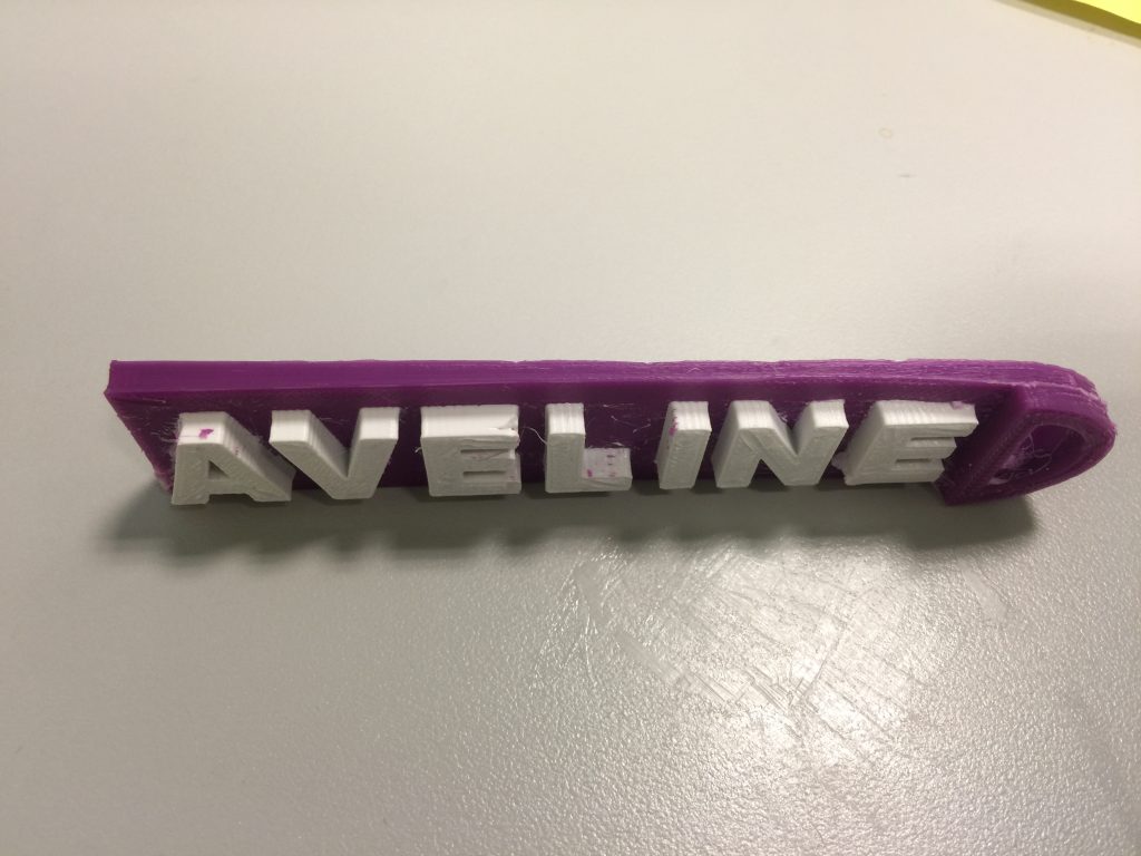 Purple and white keychain with the name A V E L I N E on it, showing some major flaws in the printing process