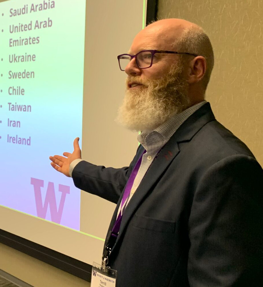 Terrill Thompson looking dapper, gesturing toward a giant projected slide that lists the many countries that are celebrating GLobal Accessibility Awareness Day