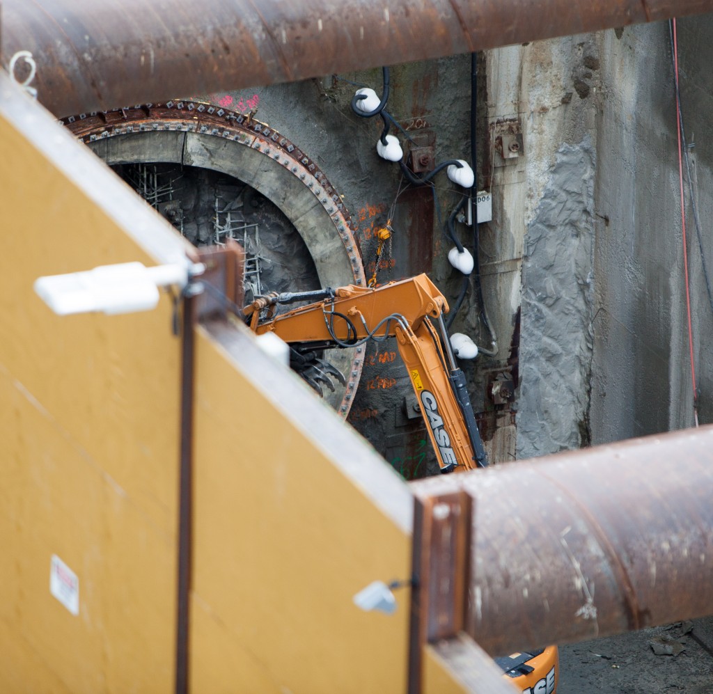 An excavator with a hydraulic breaker chipping away the pit concrete wall.