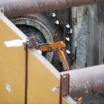 An excavator with a hydraulic breaker chipping away the pit concrete wall.